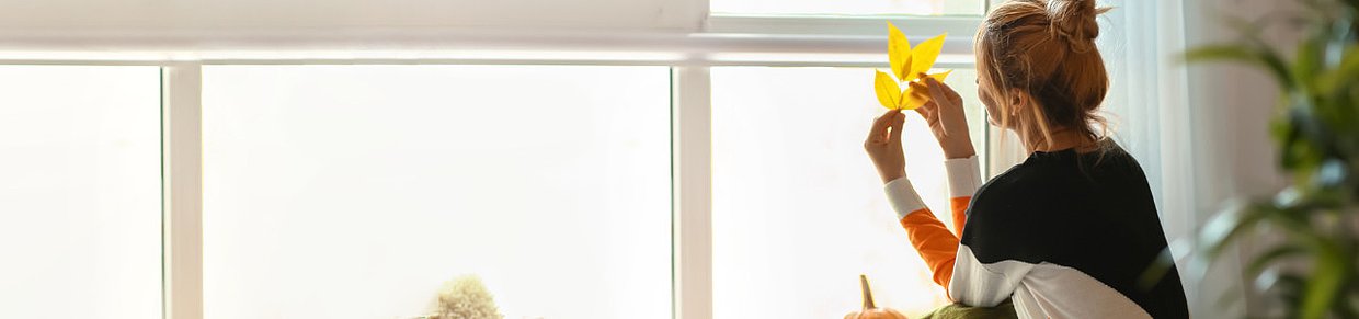 Nachdenkliche Frau mit Herbstlaub vor hellem Fenster – Symbolbild für zyklusbedingte Unfruchtbarkeit