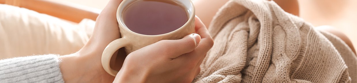 Hände mit Tasse in gemütlicher Umgebung – Symbol für Wärme und Entspannung bei Regelschmerzen/Dysmenorrhoe