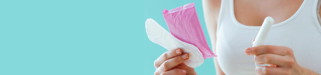 Frau hält Binde und Tampon vor türkisfarbenem Hintergrund – Symbolbild für starke Regelblutung bzw. starke Periode