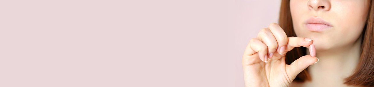 Frau hält rosa Tablette – Symbolbild für Schmerzmittel bei Regelschmerzen und PMS.