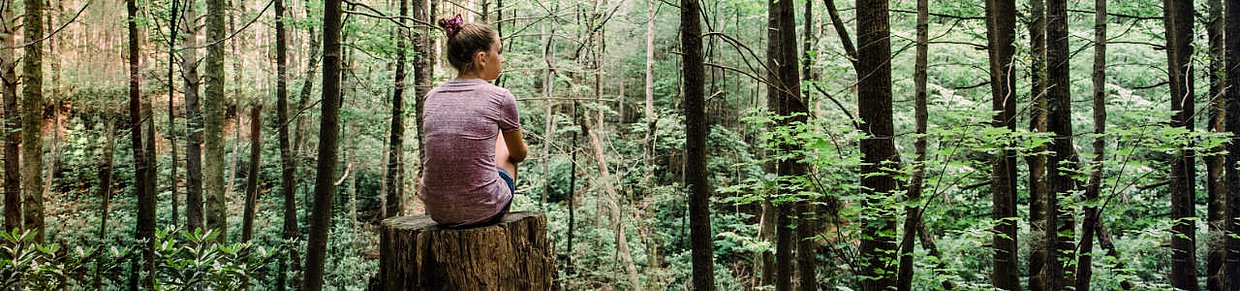 Frau sitzt allein im Wald – Symbolbild für Rückzug und depressive Symptomatik bei PMS.