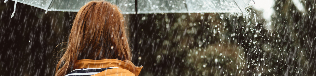 Frau geht mit Regenschirm im Regen spazieren - Symbolbild für Unterleibsschmerzen ohne Periode